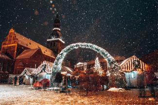 Rīga, Latvija. Ziemassvētku tirgus panorāma Doma laukumā ar Rīgas Doma baznīcu, Ziemassvētku eglīti un tirdzniecības namiņiem sniegotā naktī un krāšņiem uguņošanas šoviem. Slavenā vietzīme ziemā.