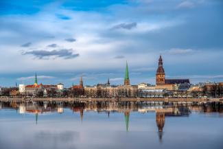 Rīgas pilsētas siluets dienas laikā. Rīgas torņi, zilas debesis un mākoņi fonā. Fotografēts no Pārdaugavas no Daugavas otra krasta. Rīgas panorāma. Latvijas galvaspilsēta.