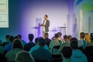 Profesionāls runātājs, kas sniedz prezentāciju auditorijai modernā konferences vidē ar rosīgu vidi un saistošu atmosfēru.